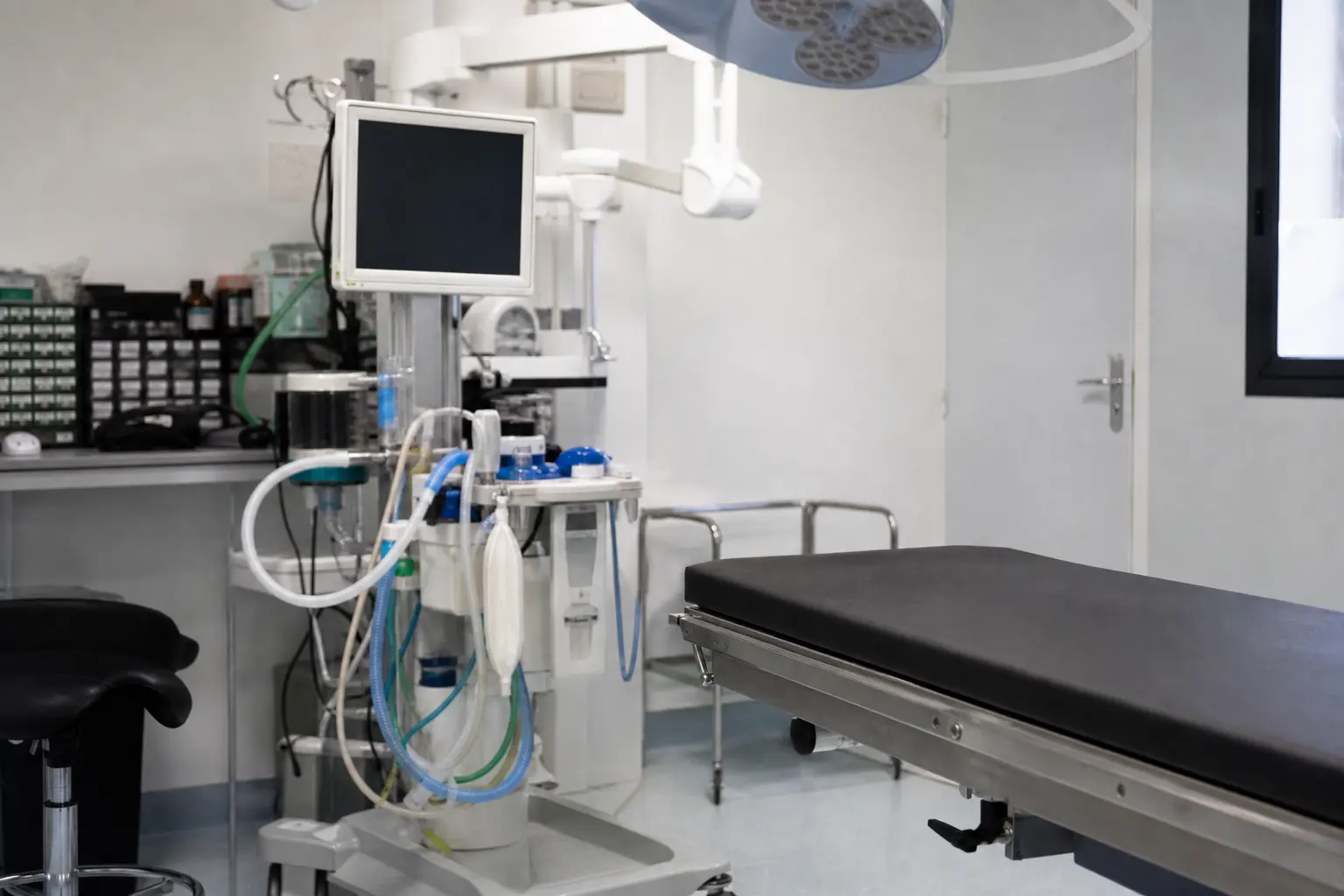 Moniteur de surveillance anesthésique et tuyaux d'anesthésie posés près d'une table d'opération vétérinaire vide, dans la lumière froide d'un bloc