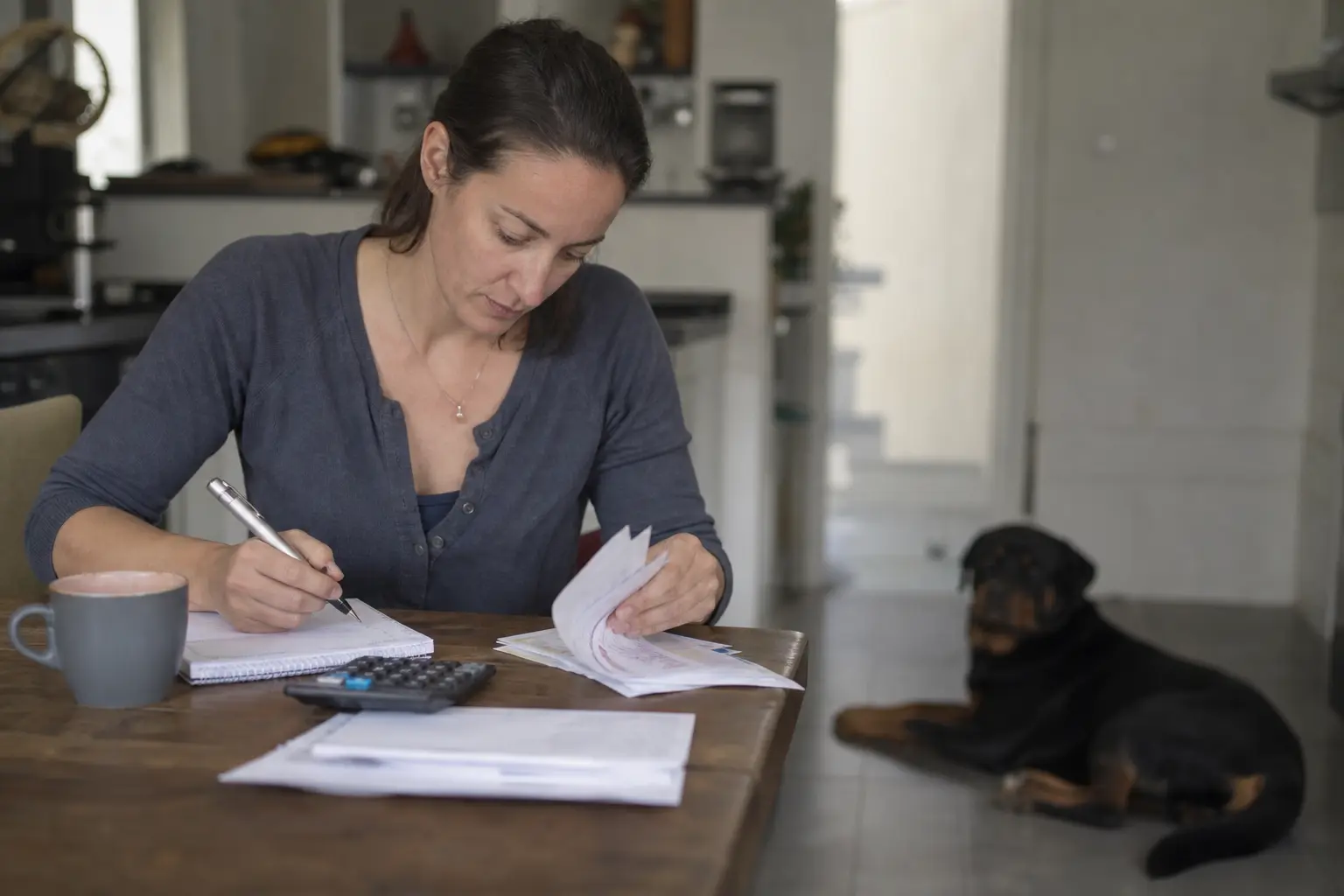 Une femme trie des factures vétérinaires avec une calculatrice à la table de sa cuisine