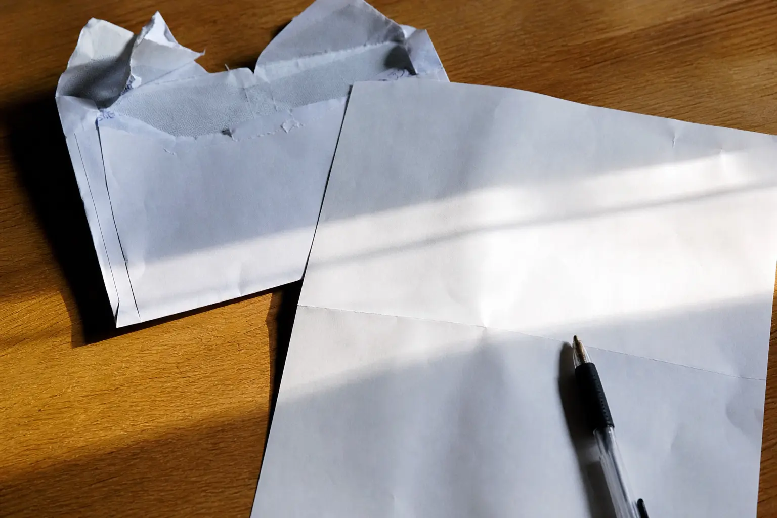 Une enveloppe recommandée ouverte et un courrier administratif posés sur une table avec un stylo, dans une lumière naturelle rasante