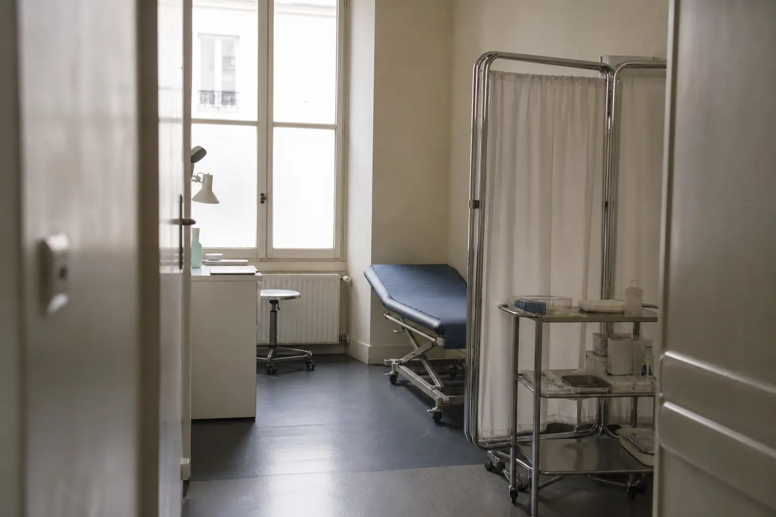 Une salle d'examen médicale vide avec une table, un paravent et un plateau de pansements et de compresses préparés