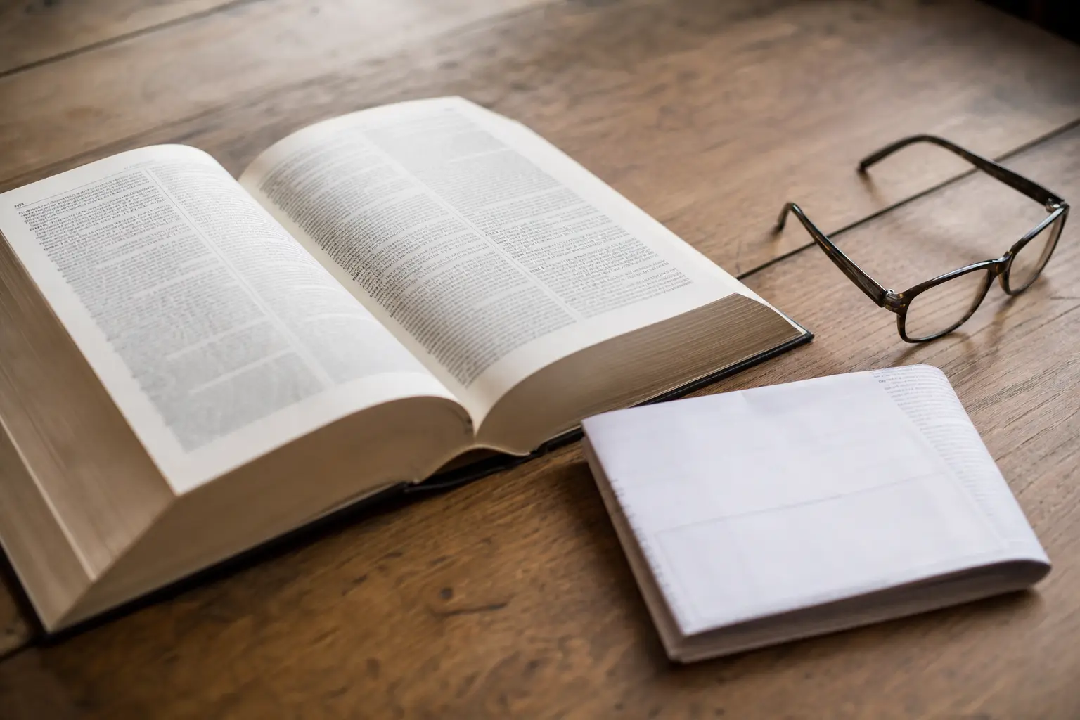 Un dictionnaire ouvert à plat sur un bureau, à côté d'un contrat d'assurance plié et d'une paire de lunettes