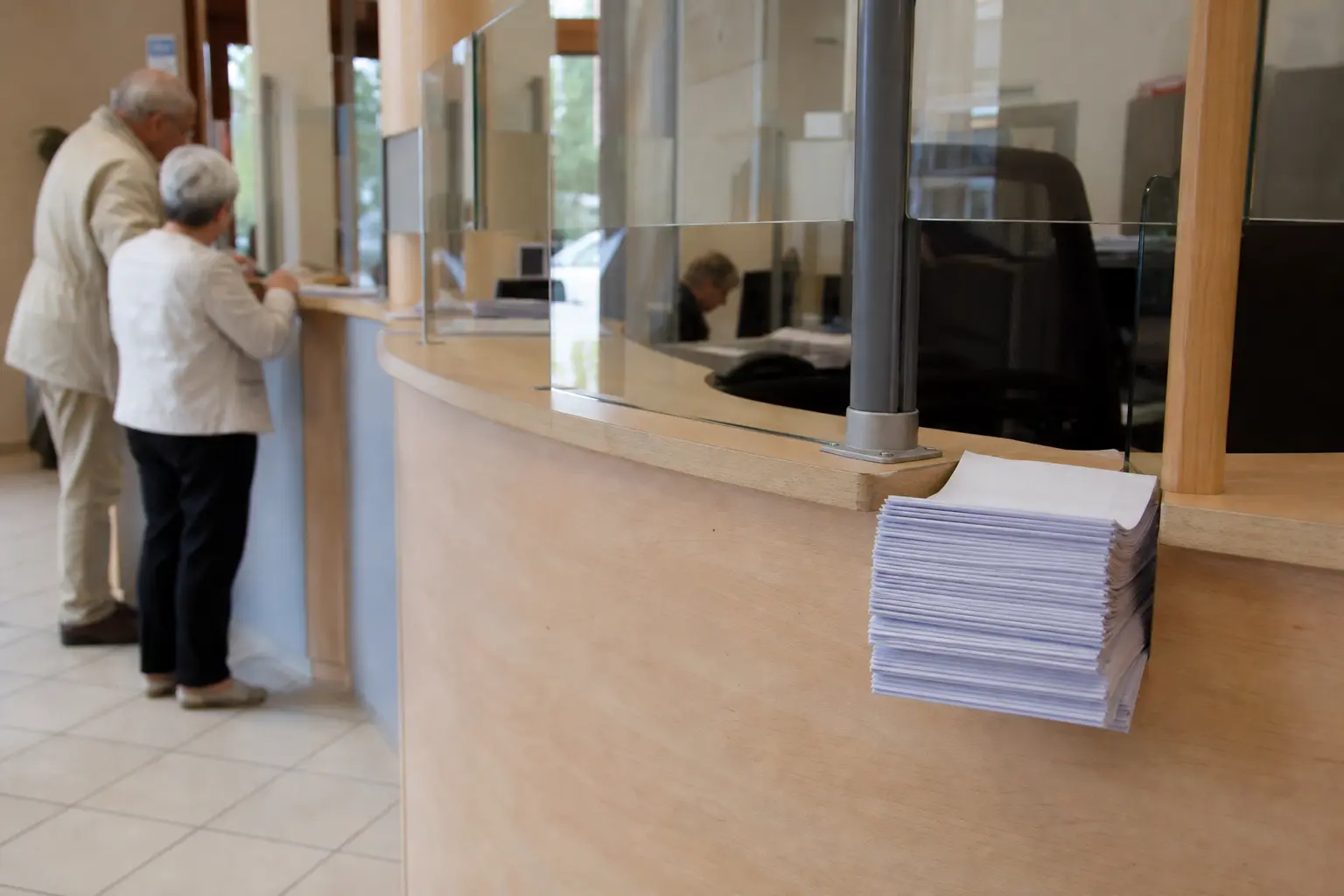 Guichet d'accueil d'une mairie avec un comptoir en bois clair et une pile de formulaires vierges